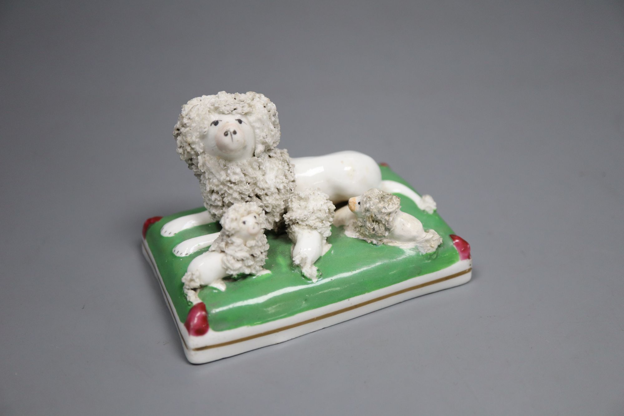 A Staffordshire porcelain group of a poodle and three puppies on a green cushion, c.1835-50, 9cm long